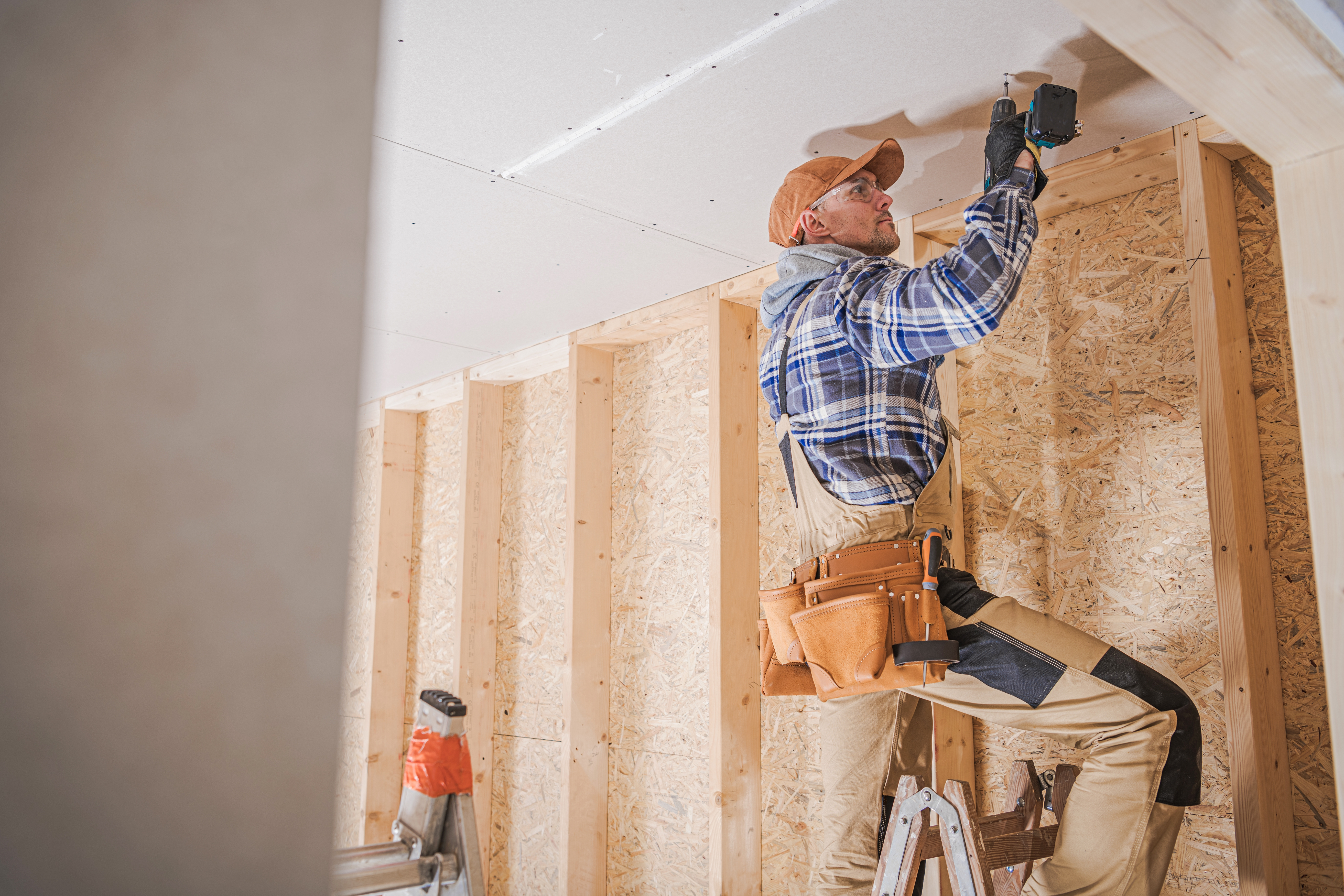 Tradesperson installing drywall on a framed structure